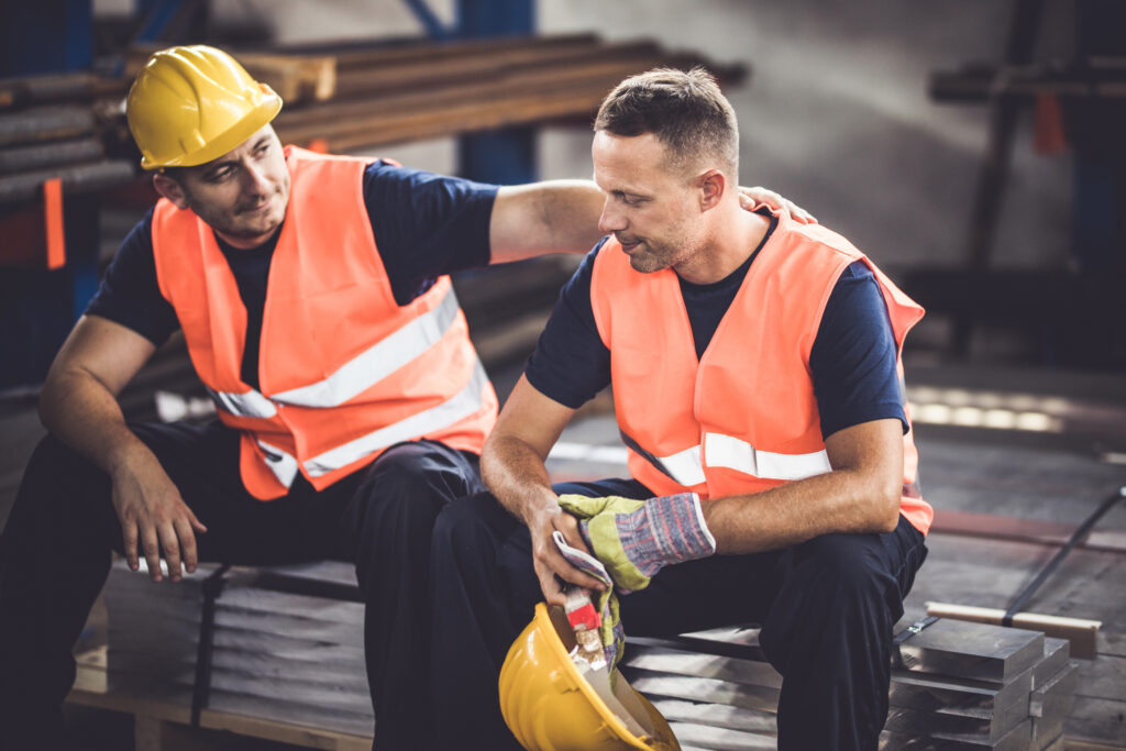 Sad manual worker being consoled by his colleague in aluminium mill.