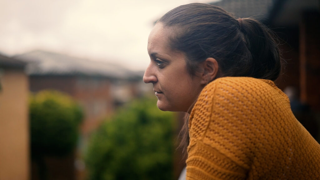 Christine wearing an orange jumper and looking over a balcony