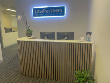 Reception area of the Ringwood office. The front desk has an orchid on the left and Law Partners fliers on the right. There is a blue sign on the wall that says Law Partners in white writing.