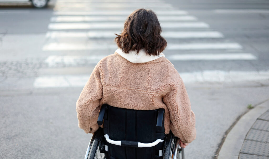 Woman with back injury in a wheelchair crossing the street in a city. About 30 years old, Caucasian female.
