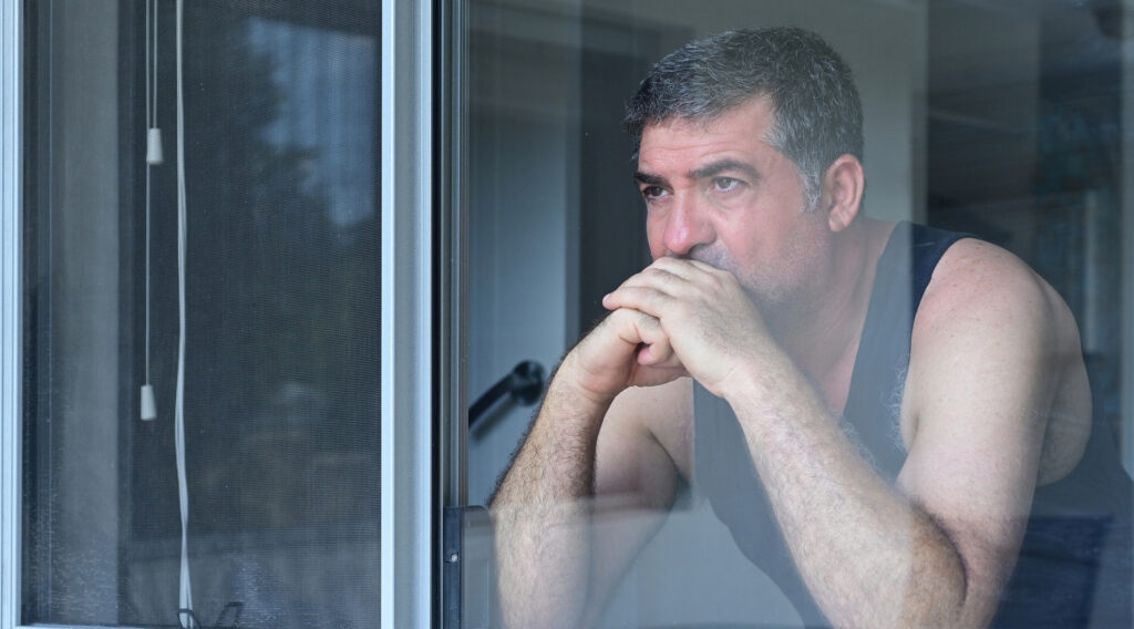 Sad middle-aged man, looking out the window of his home. 