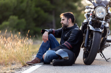 Motorcyclist sitting by the road leaning on motorcycle